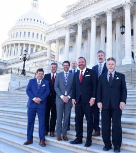 Men in suits pose with the U.S. Capitol in the background.