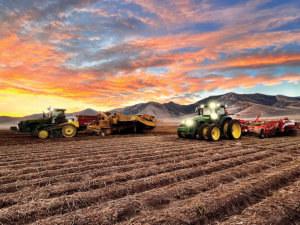 tractors wait to plow another row under a sunset of brilliant pink and blue