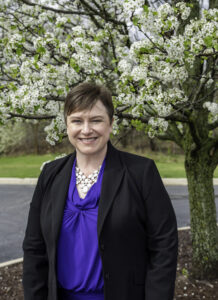 Woman in black blazer smiling in front of flowering tree