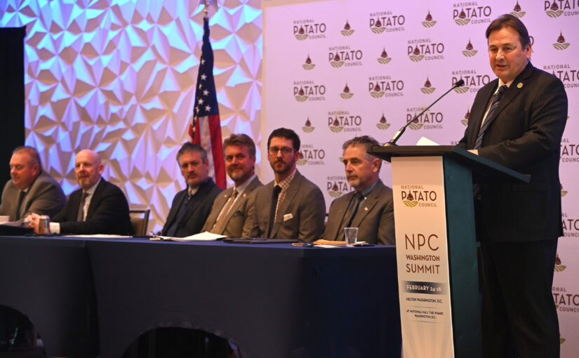 Ted Tschirky, the new NPC president, speaks at a podium as a group of committee members look on
