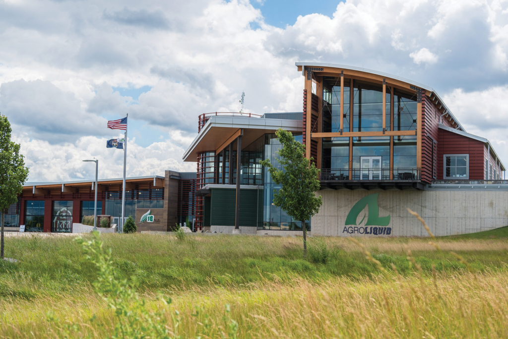 A glass-and-brick building rises above green grass against white clouds