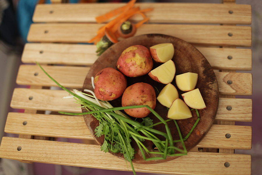 Sliced potatoes on a plate next to whole potatoes and green vegetables