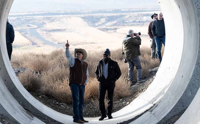 A group of men stand in the opening of a large irrigation pipe