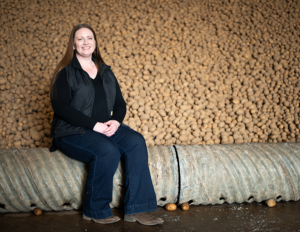 A smiling woman sits in front of a bank of stored potatoes