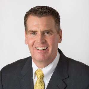 head shot of man in dark suit with yellow tie