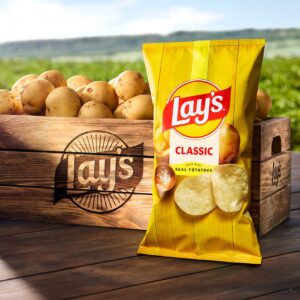 A bag of Lay's potato chips, featuring a redesigned logo with sunbeams, beside a crate of potatoes