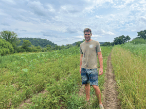 A man poses in between rows of potatoes 