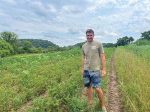 A man poses in between rows of potatoes 