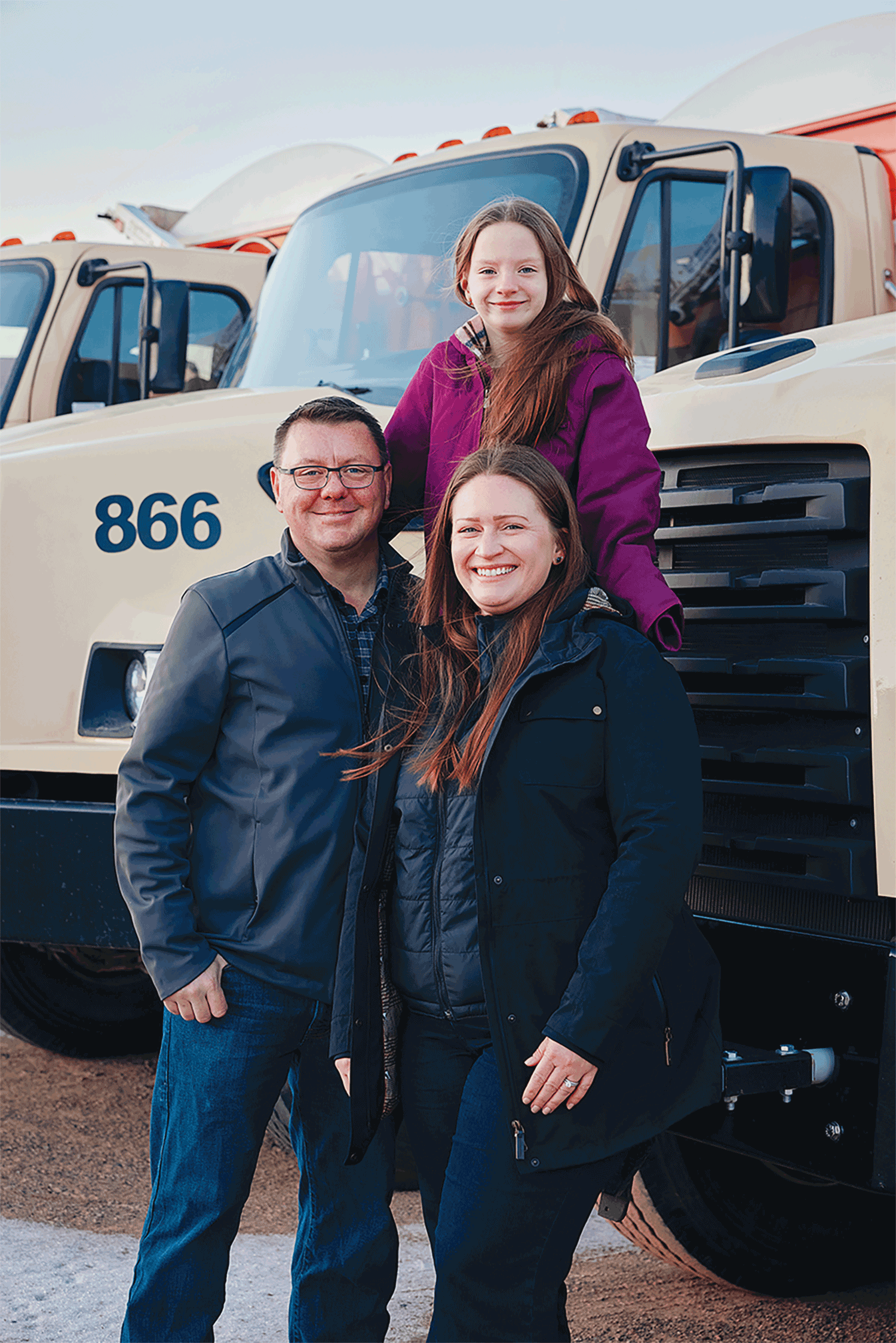 A family of three - dad, daughter and mom - poses in front of a large truck. 