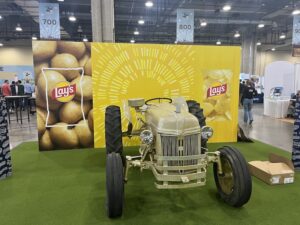 A vintage tractor is positioned in front of a Frito Lay display on the Potato Expo 2026 show floor.