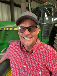 Headshot of smiling man standing in front of farm equipment