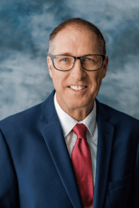 Headshot of smiling man in dark jacket and red tie