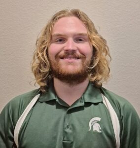 Head shot of man with blond hair and a beard in an MSU logo shirt