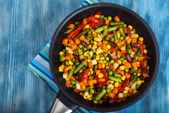 A pan of freshly sauteed vegetables including carrots, corn and snap peas